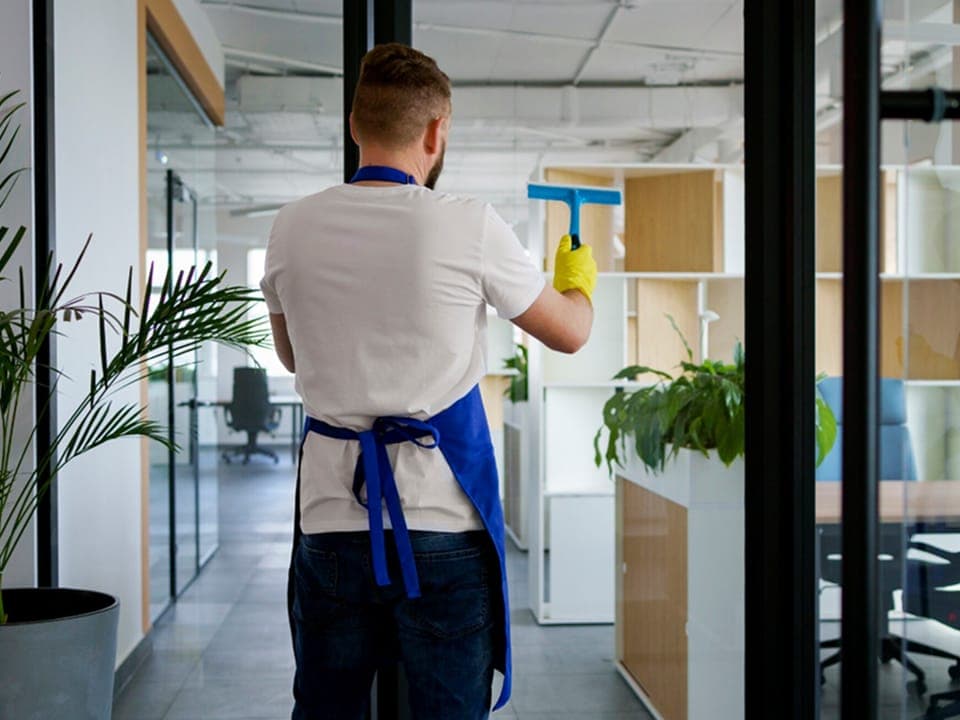 A cleaner squeegeeing a glass partition in an open-plan commercial space