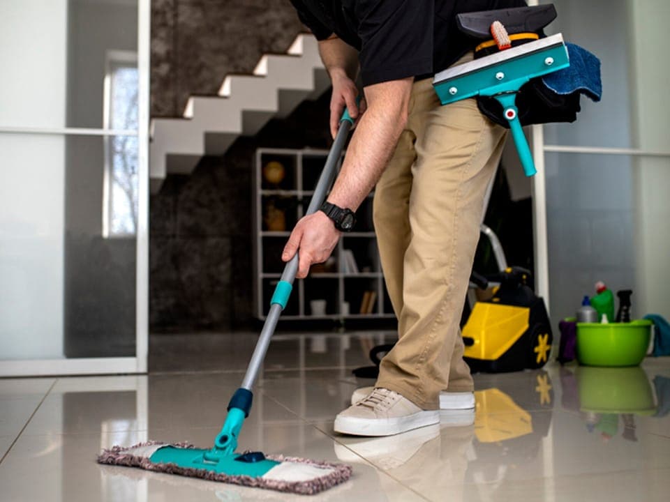 A cleaner mopping a polished tile floor in a private home, equipment cart behind